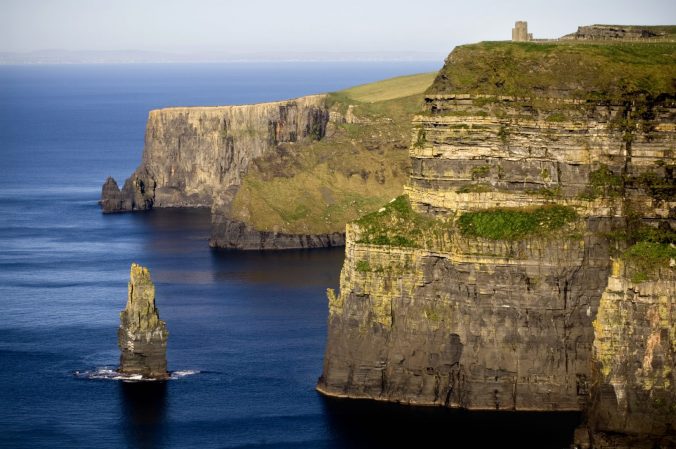 A stone bridge over a body of water with Cliffs of Moher in the background