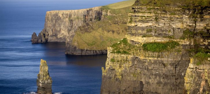 A stone bridge over a body of water with Cliffs of Moher in the background